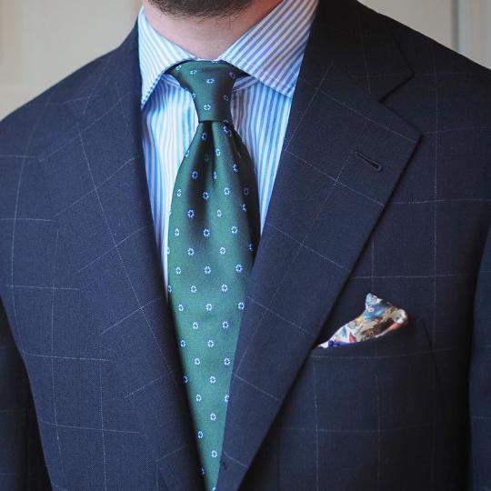 Tamsiai mėlynas languotas švarkas, šviesiai mėlyni dryžuoti marškiniai, žalias margas kaklaraištis