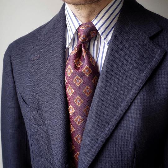 Tamsiai mėlynas švarkas, balti mėlyni dryžuoti marškiniai, violetinis raštuotas kaklaraištis