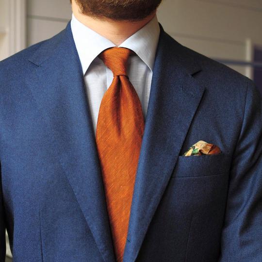 Mėlynas švarkas, balti marškiniai, oranžinis kaklaraištis