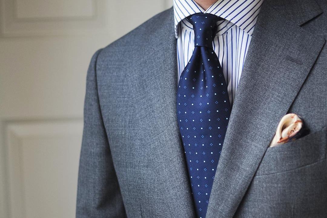 Pilkas kostiumas, mėlyni juostuoti marškiniai, mėlynas taškuotas kaklaraištis