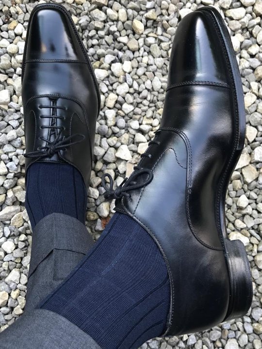 Pilkos kelnės, tamsiai mėlynos kojinės ir juodi batai